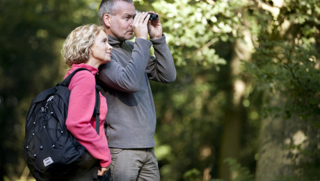 Mature couple standing in the countryside, man looking through binoculars